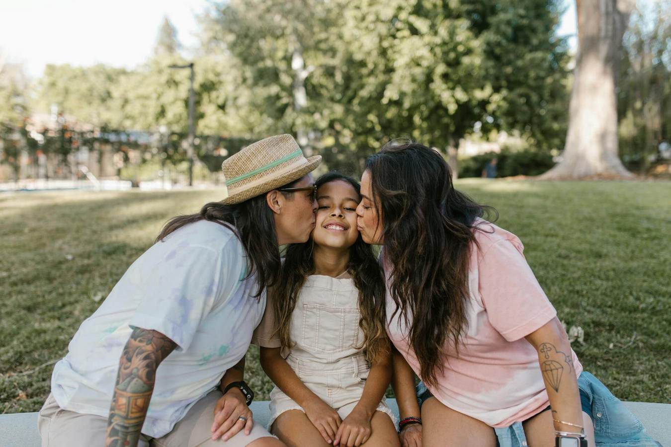 Lesbian couple share a kiss with their daughter in a par